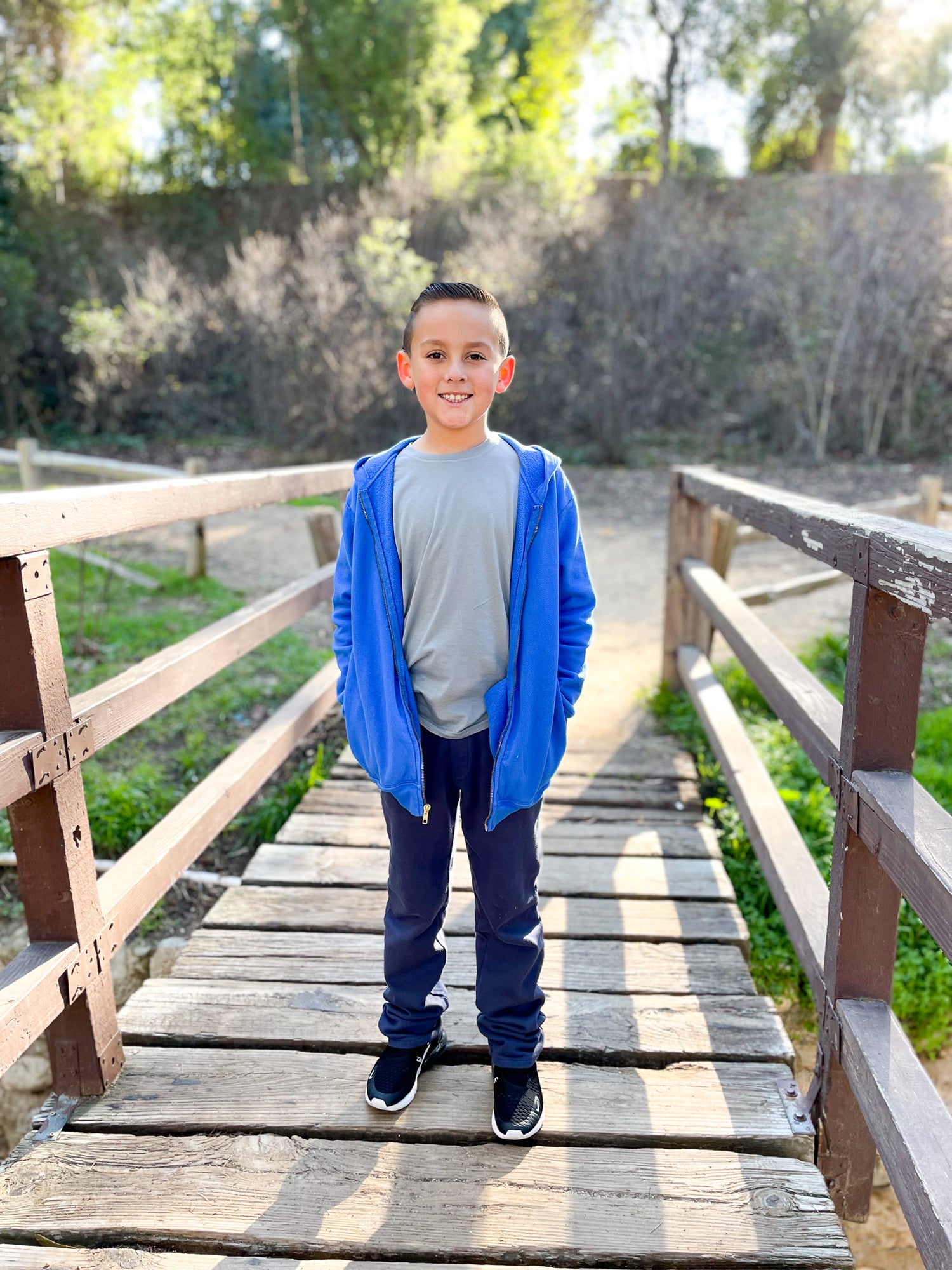 Boy standing on bridge wearing a zip up hoodie and fleece pants.