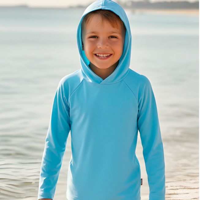 Child wearing a blue hoodie standing on a beach.