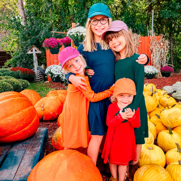 Woman with three children in a pumpkin patch surrounded by pumpkins and flowers.