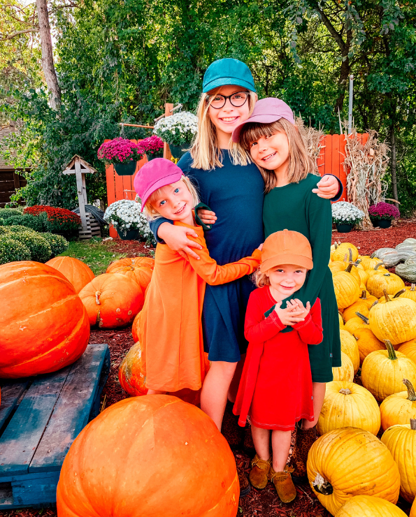 Woman with three children in a pumpkin patch surrounded by pumpkins and flowers.