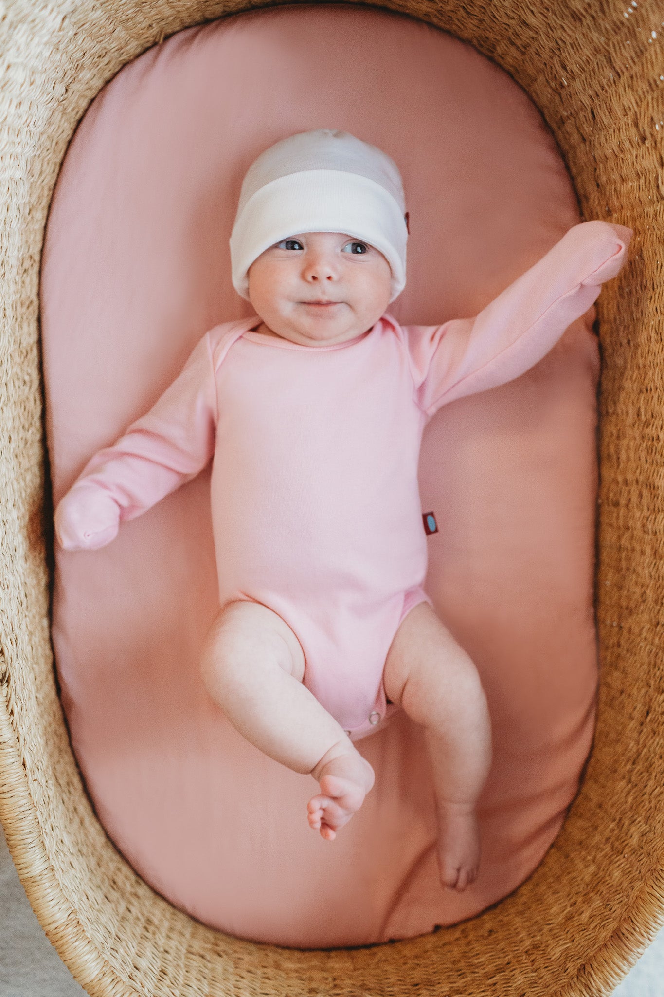 Baby laying comfortably in a bassinet wearing organic cotton long sleeve onesie