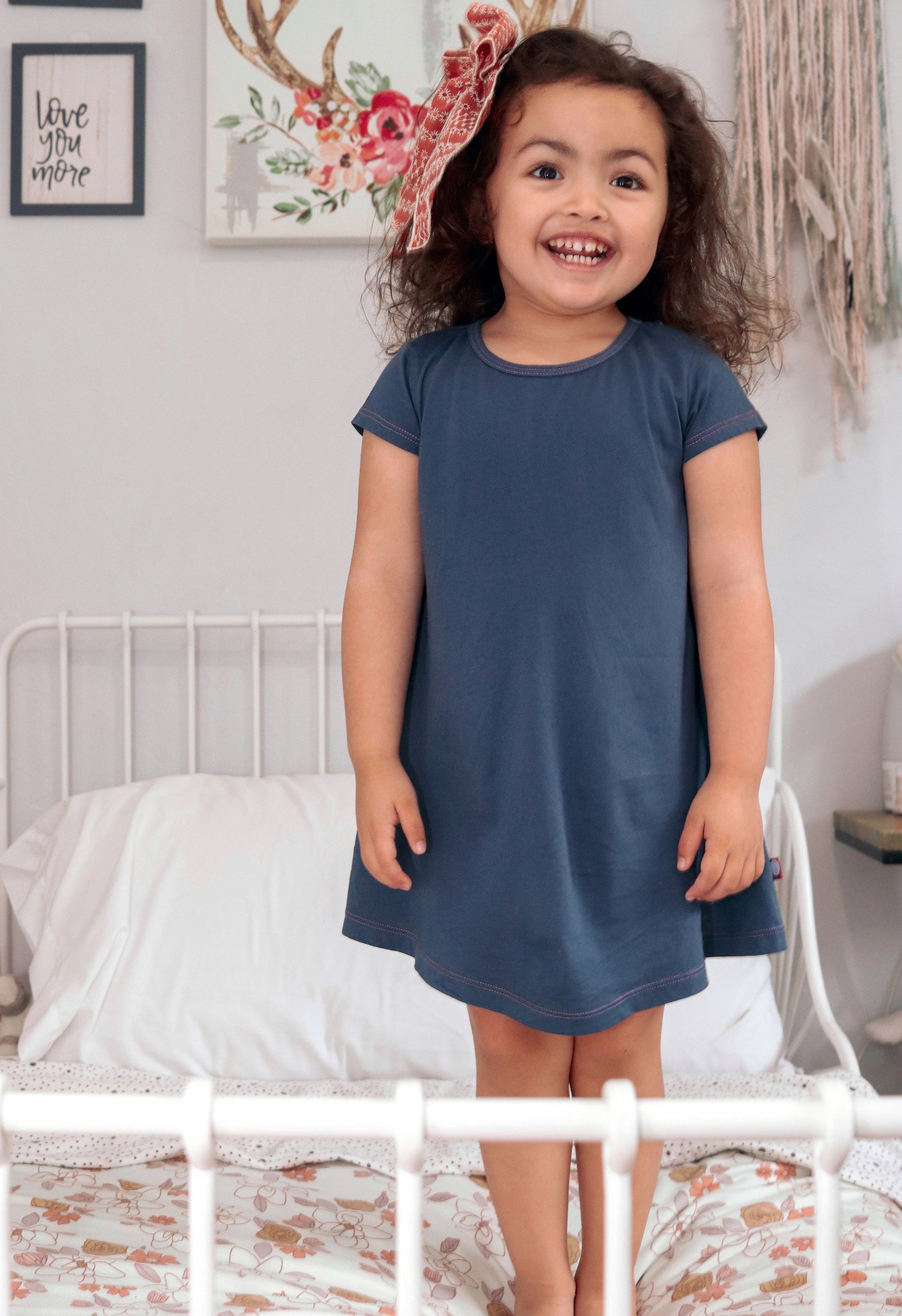 Girl in a short sleeve dress standing on a bed.