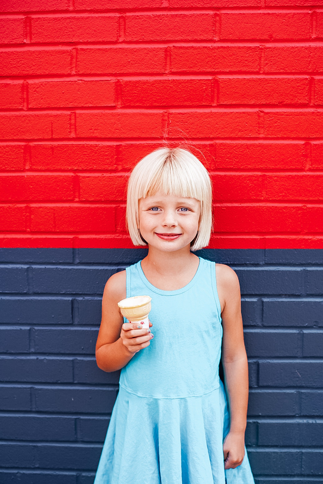 Girl eating an ice cream cone in a tank dress.